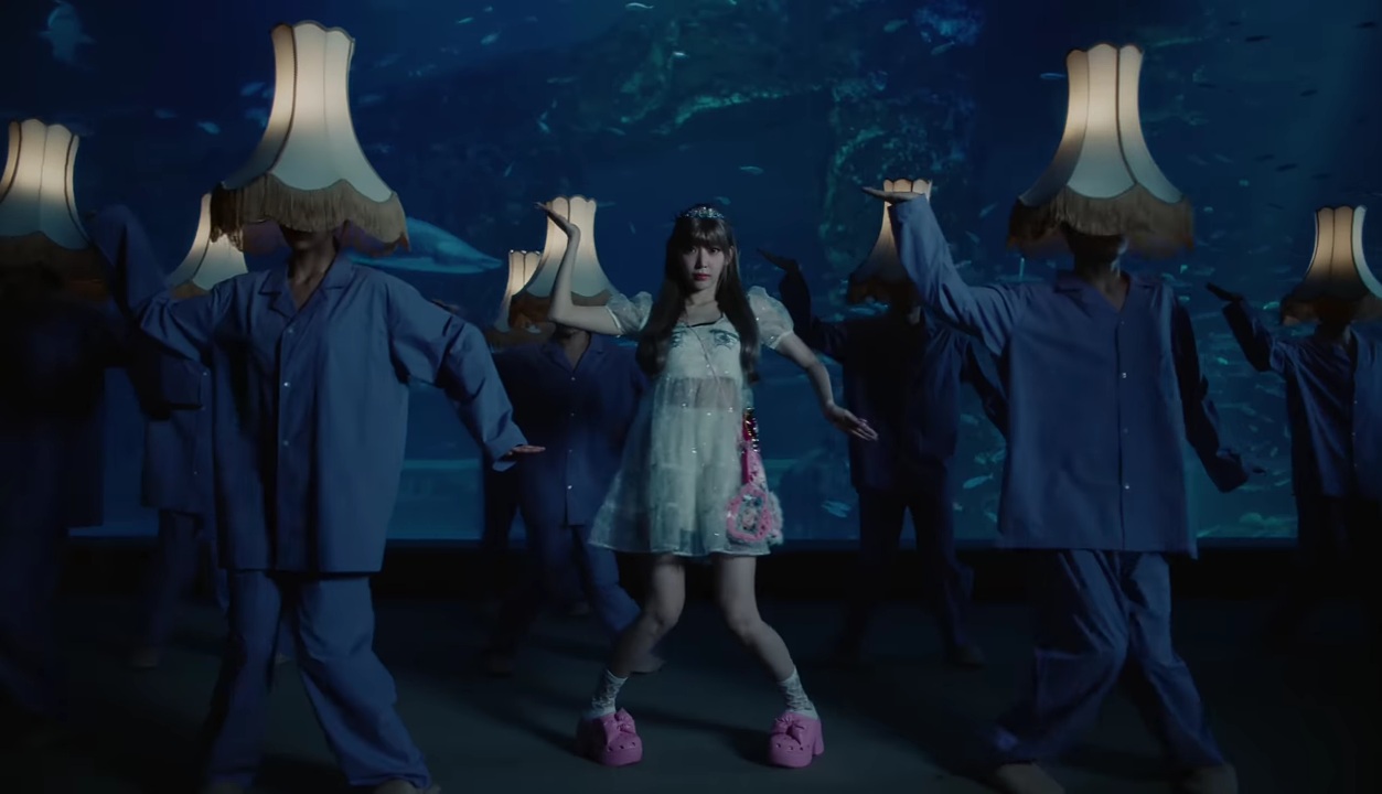 LE SSERAFIM's Sakura playing around with dancers wearing lampshades on their heads in the music video for CRAZY.