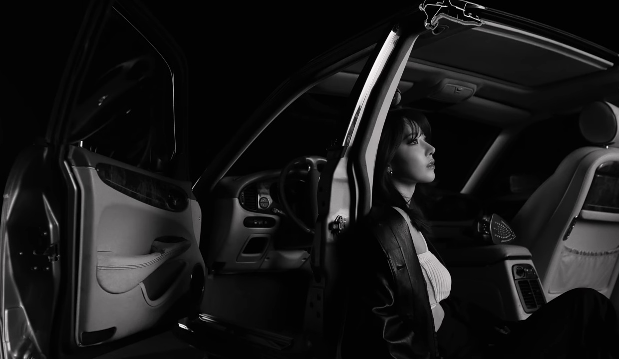 A black and white photo of LE SSERAFIM's Sakura sitting in a car from the group's HOT music video.