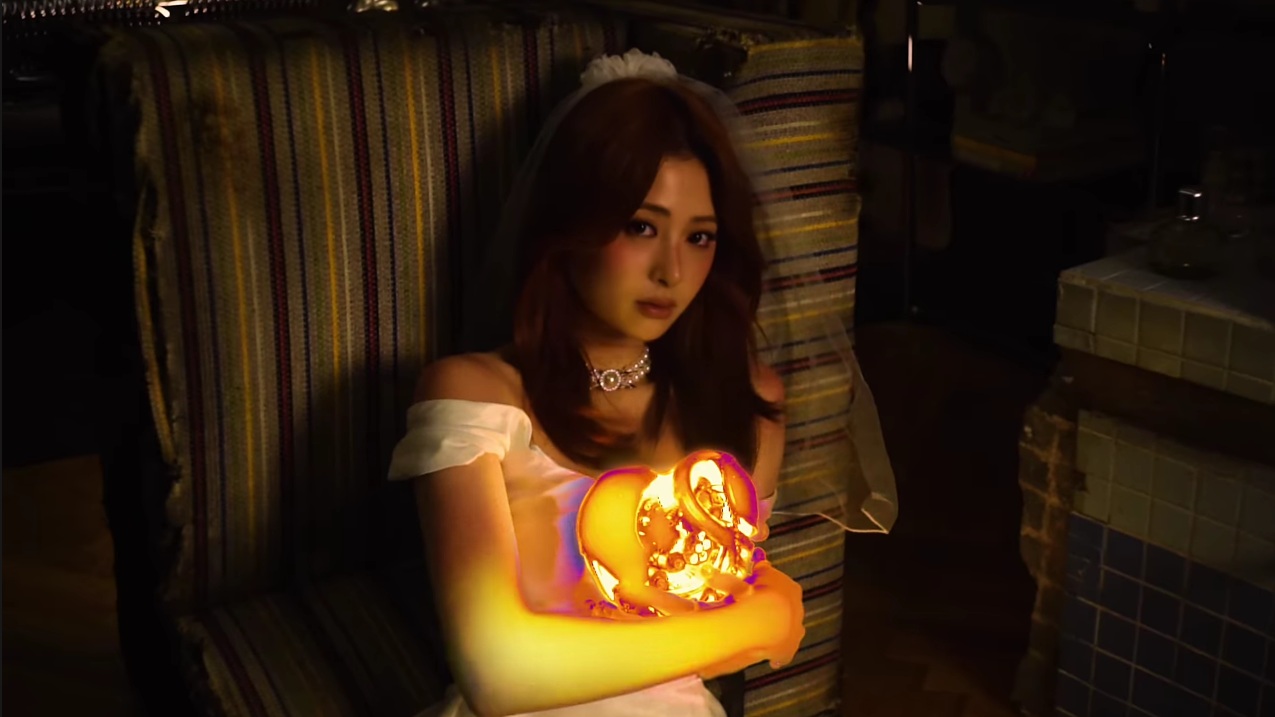 LE SSERAFIM's Huh Yunjin is holding a glowing heart-shaped engine stained in crimson from the HOT music video.